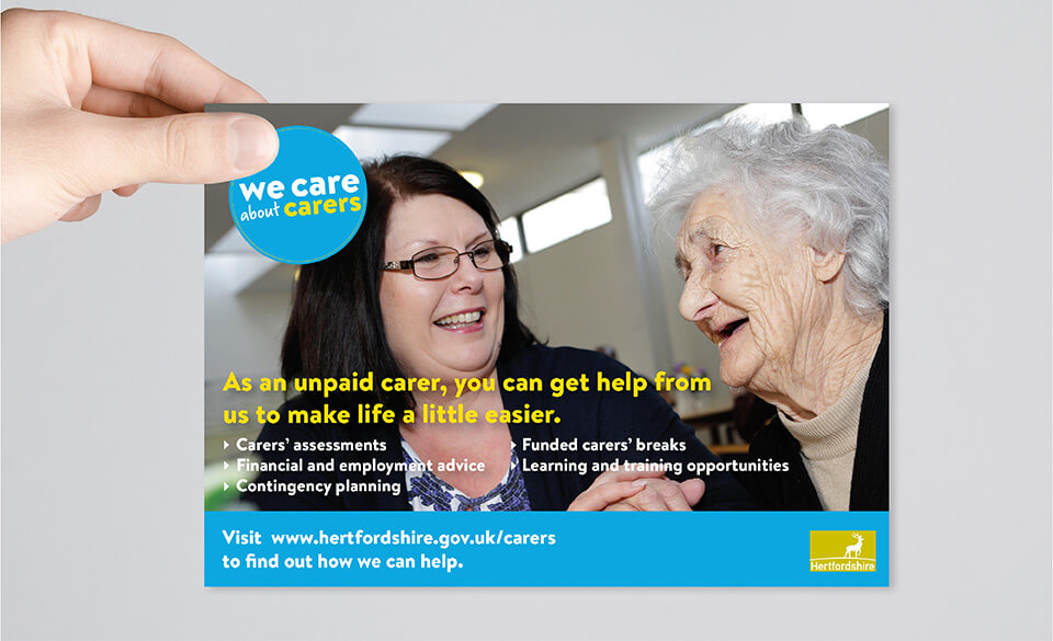 A hand holding up a flyer depicting an elderly care user and her carer.