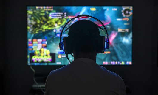 A man wearing a gaming headset playing a game on a large computer screen.
