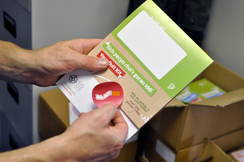 A man places a sticker seal onto one of the printed Quit Kits from the Quit for Them campaign.