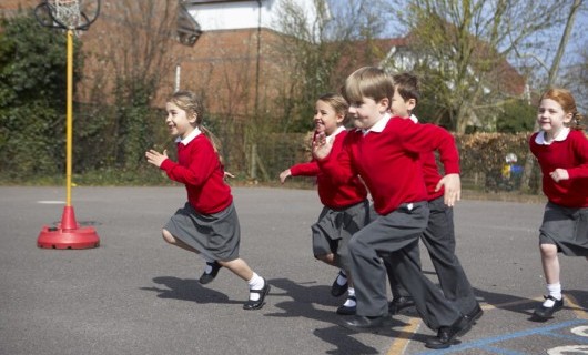 A group of school children in red jumpers running across the school's playground.